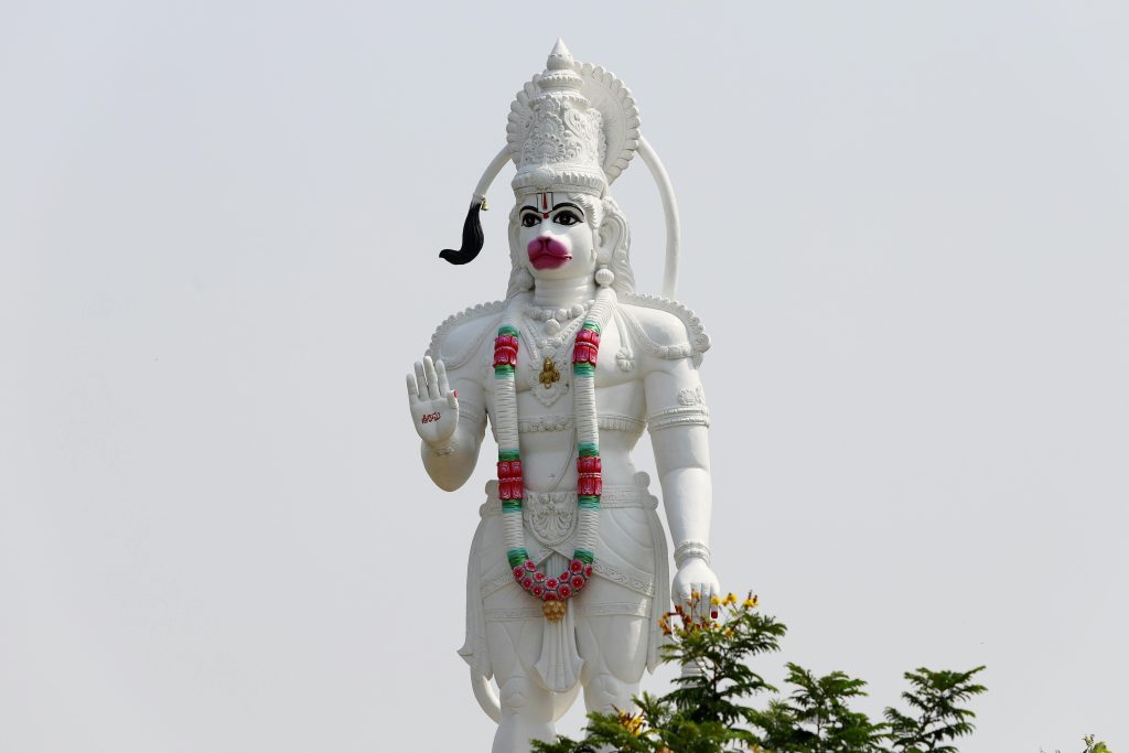 Large white Hanuman statue adorned with colorful garlands, set against a clear sky.